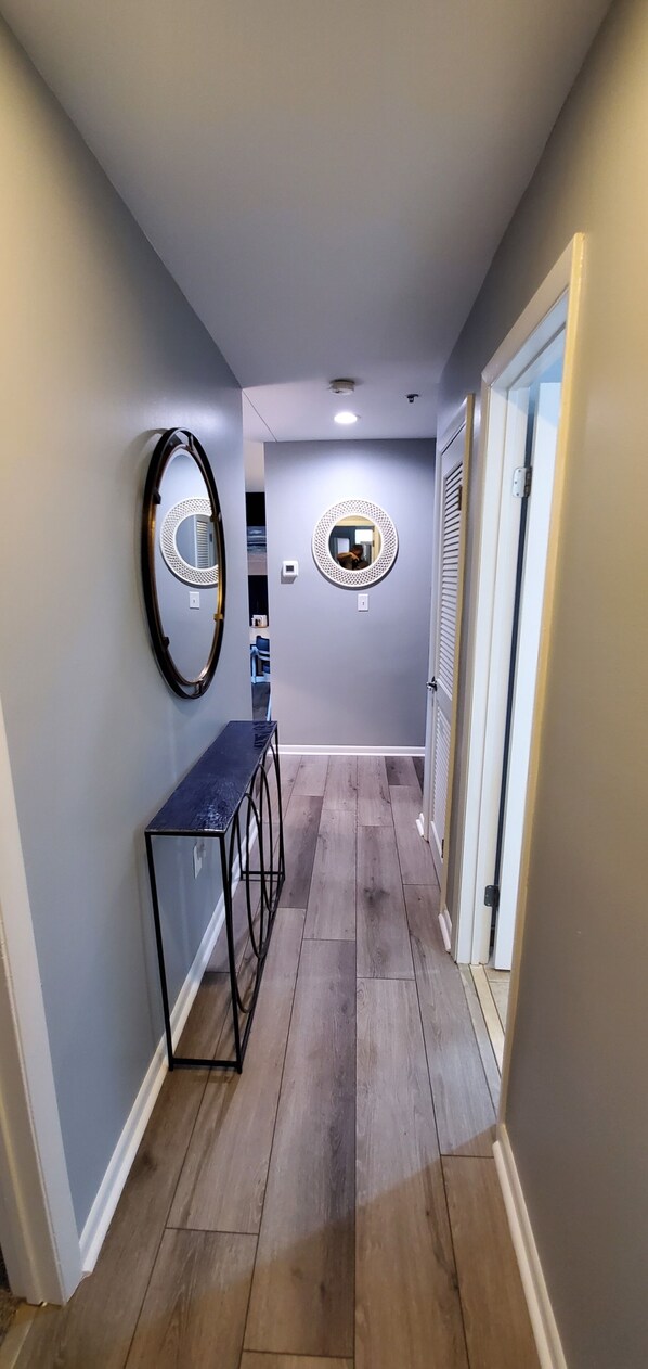 A hallway with a console table, two wall-mounted mirrors, and a door leading to another room. - Modern 2 bedroom, 2 full bathroom, with elevator in the heart of everything VB, (Virginia Beach)
