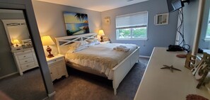 A bedroom with a bed, bedside tables, a desk, a window with blinds, a painting, and a mirror. - Modern 2 bedroom, 2 full bathroom, with elevator in the heart of everything VB, (Virginia Beach)