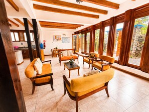 A spacious living area with wooden furniture, large windows, and a kitchen in the background. - Modern, Spacious House with a Cozy Atmosphere and an Excellent Location (Puerto Ayora)