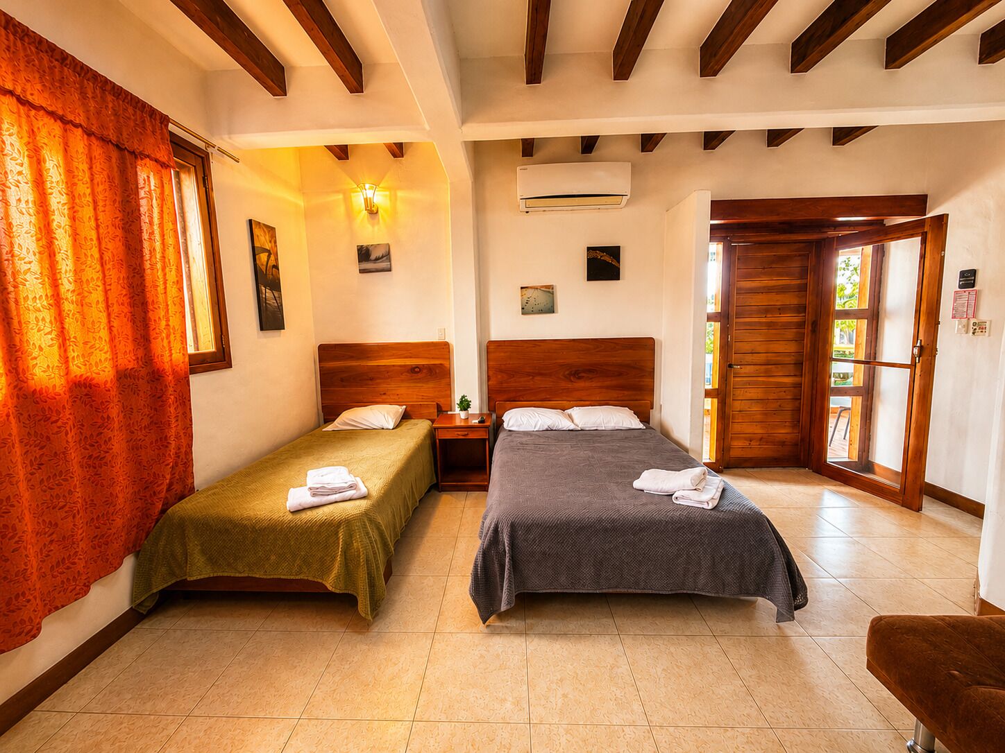 A room with two beds, a wooden ceiling, an air conditioning unit, and a door leading outside.