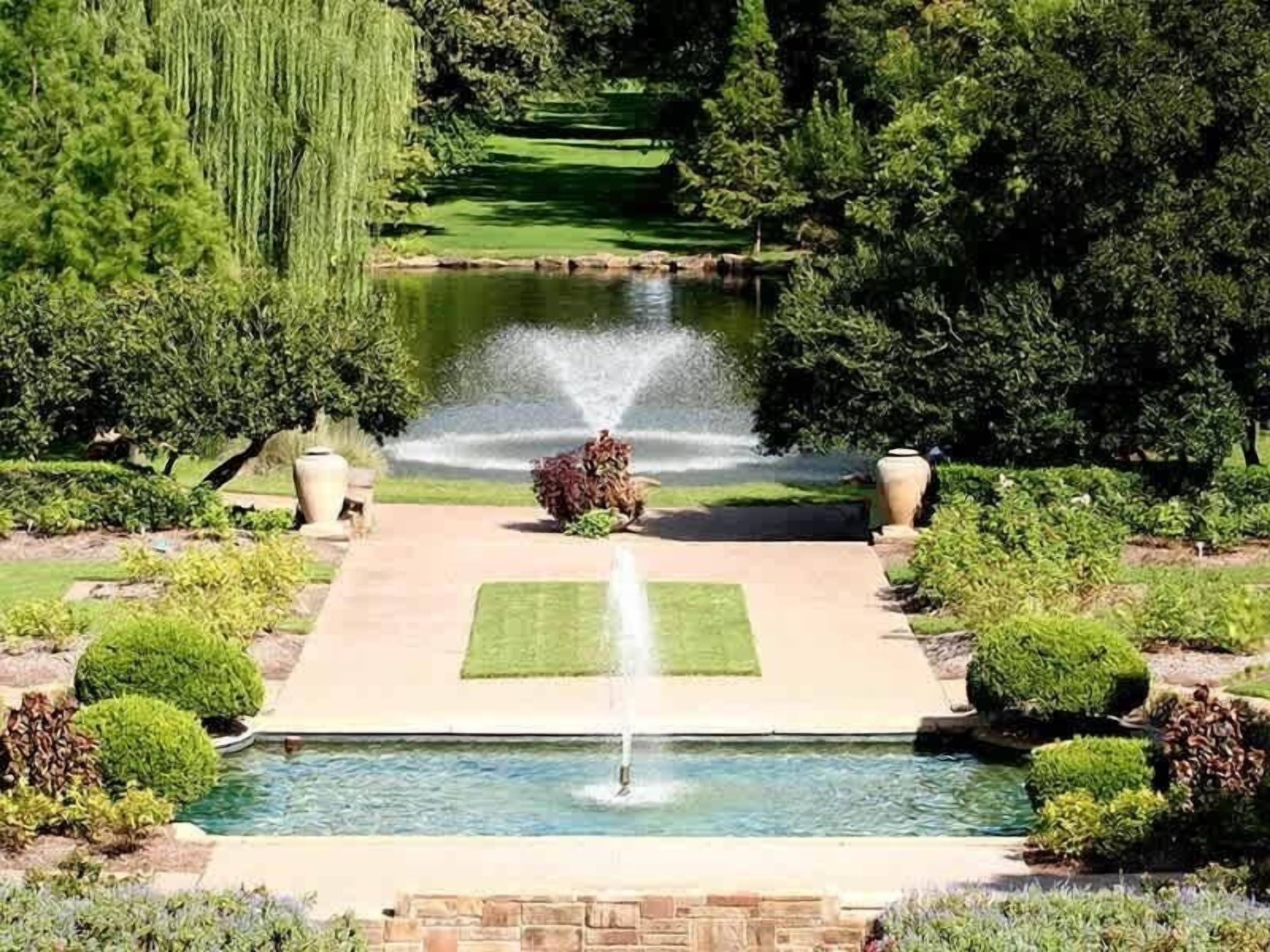 Een aangelegde tuin met een centrale fontein, een zwembad en een fraai onderhouden gazon.