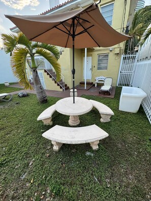 Eine Terrasse mit einem Steintisch und -stühlen, einem großen Sonnenschirm und einer Palme.
