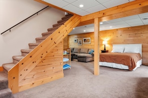 Un dormitorio con una escalera de madera, una cama, una mesita de noche, una lámpara, un sofá y una pequeña mesa con una lámpara.