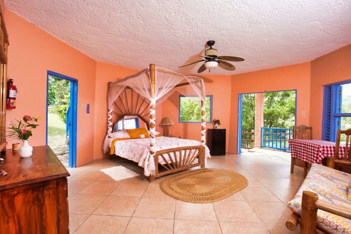 A bedroom with a four-poster bed, a ceiling fan, and a view of the outdoors.