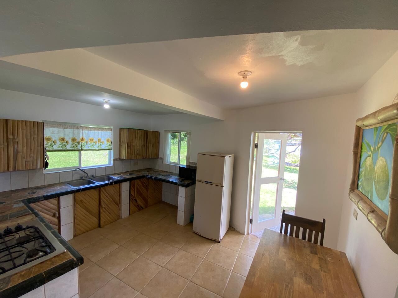 A kitchen with a gas stove, a refrigerator, a sink, and a window with curtains.