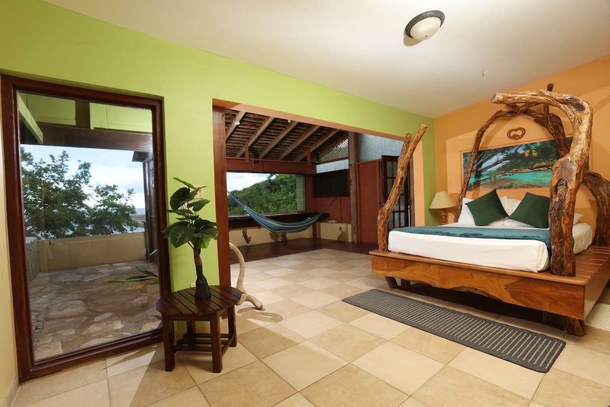A bedroom with a hammock, a wooden bed frame, and a view of the outdoors.