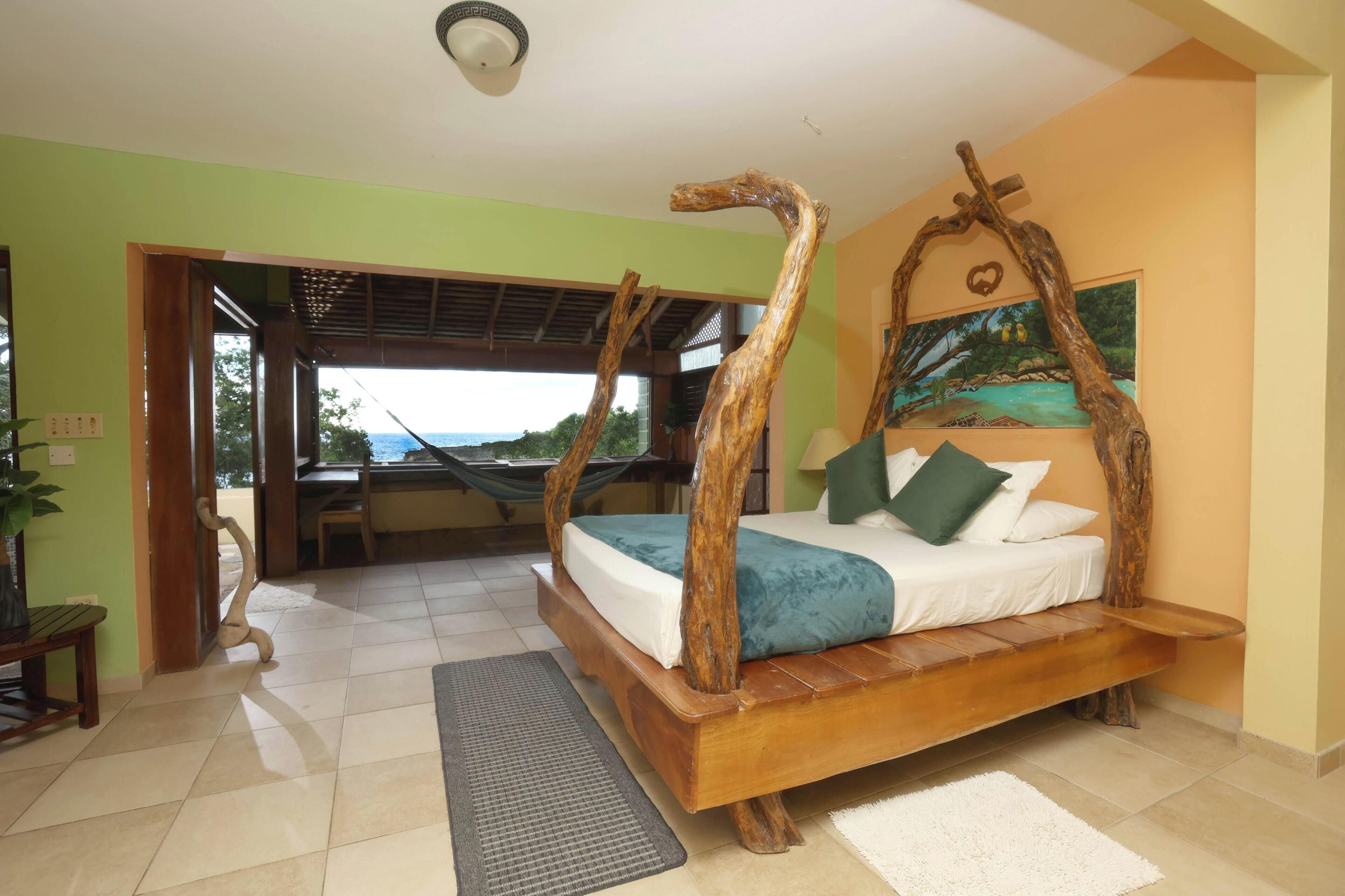 Un dormitorio con una cama con dosel de madera, vistas a través de una puerta abierta y una hamaca en la habitación contigua.