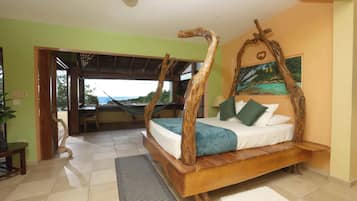 Un dormitorio con una cama con dosel de madera, vistas a través de una puerta abierta y una hamaca en la habitación contigua.