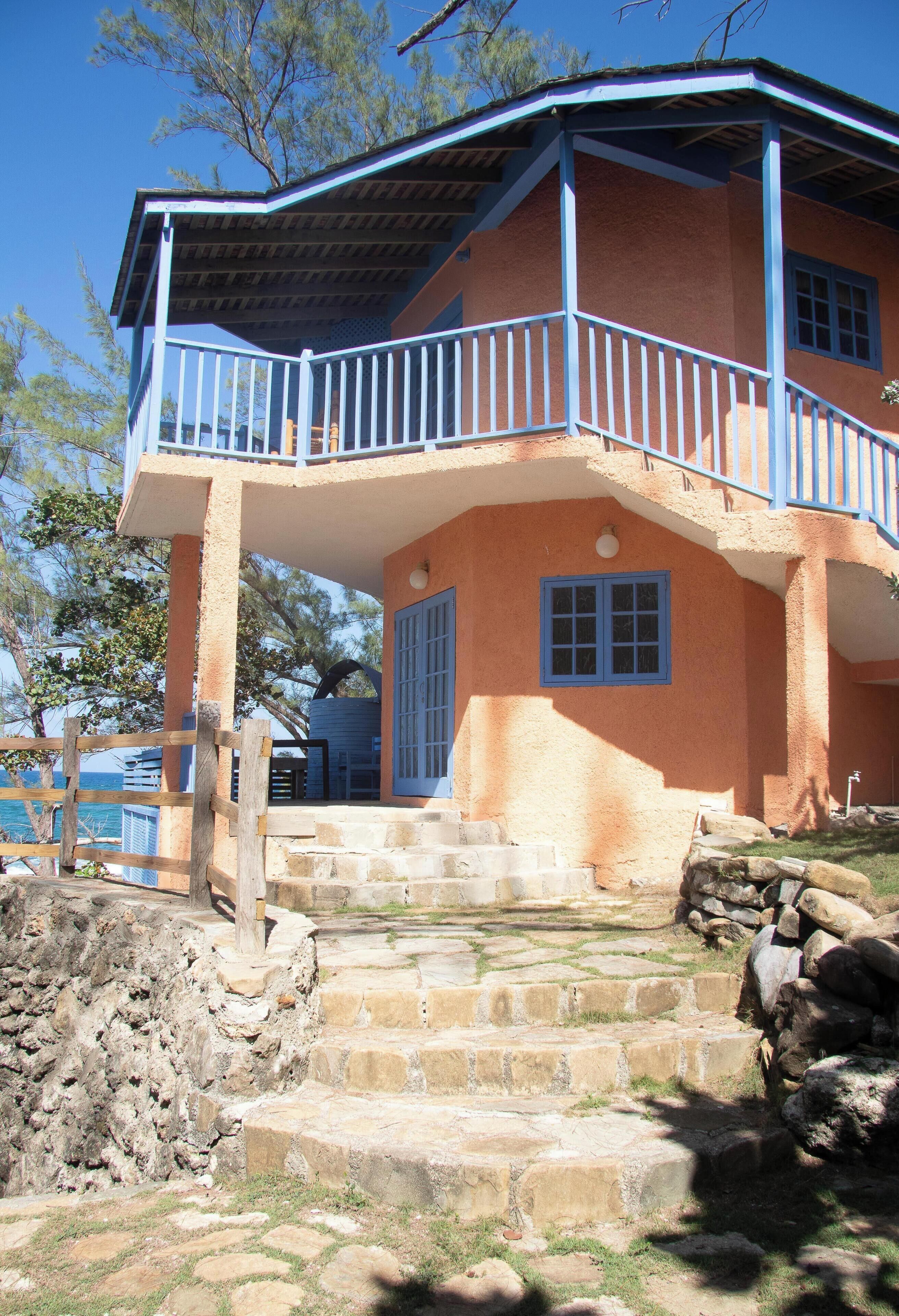 Un edificio de dos pisos con balcón, escalones de piedra y vista al mar.