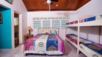 A room with a bed, a ceiling fan, a window with blinds, and a door leading to a bathroom.