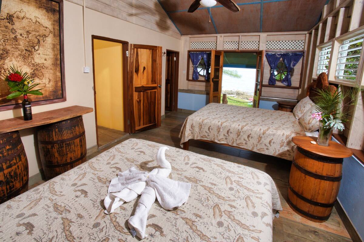 A room with a bed, a bench, a map on the wall, and a window with curtains.