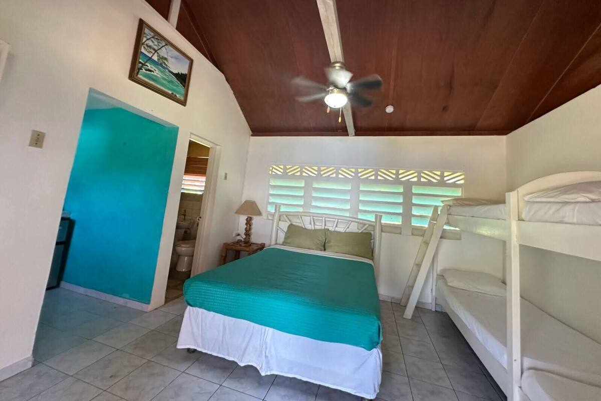 A bedroom with a bed, bunk beds, a ceiling fan, a window with blinds, and a door leading to a bathroom.