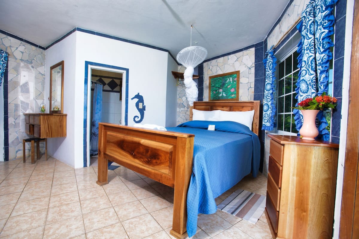 A bedroom with a wooden bed, a wooden dresser, a mirror, a door, and a window with curtains.