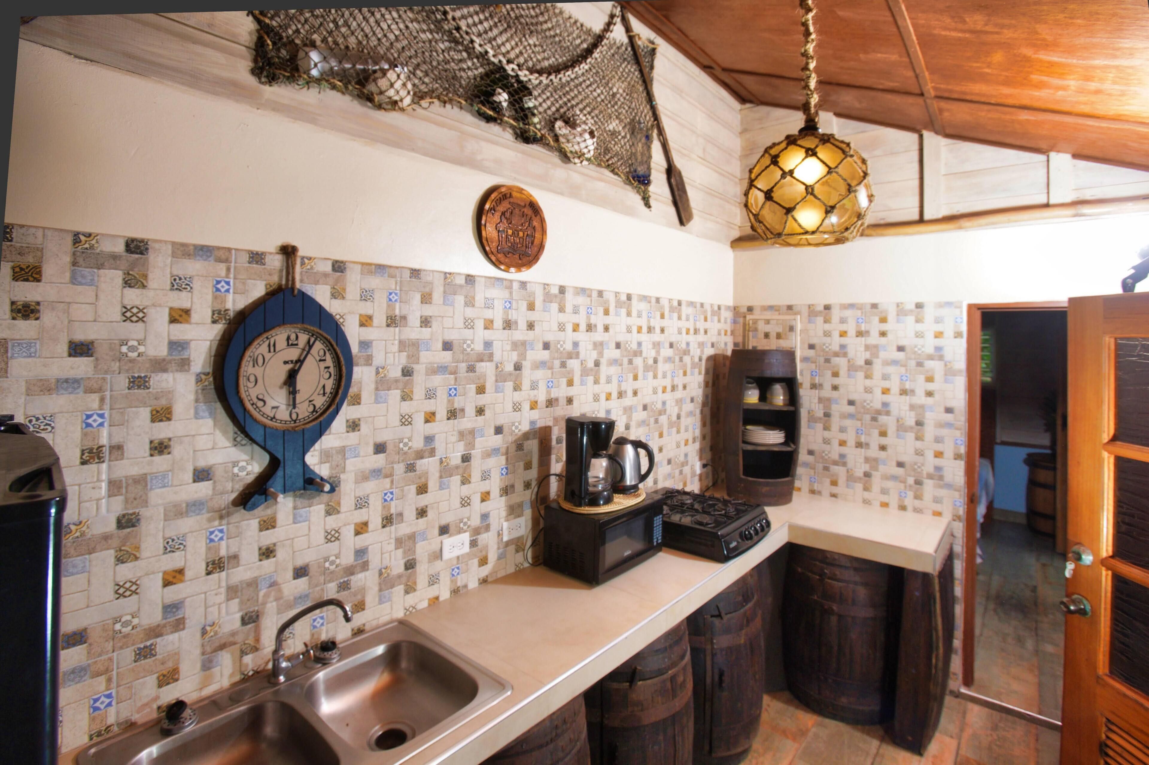 A kitchen with a tiled backsplash, a coffee maker, a clock, and wooden barrels.