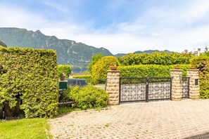 Ein gepflasterter Weg führt zu einem verschlossenen Eingang, mit Bergen im Hintergrund.