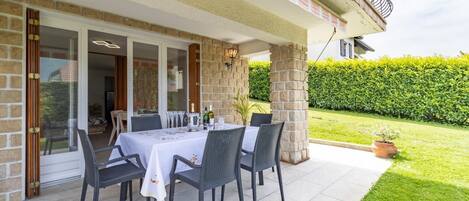 An outdoor patio with a table set for six, surrounded by wicker chairs, against a stone wall.