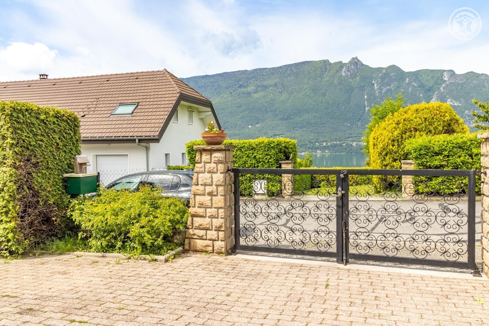 A house with a paved driveway, a gated entrance, and a mountain backdrop.