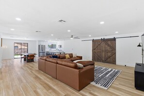 A spacious living area with a brown leather sofa, a dining table, and a kitchen in the background.