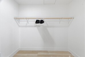 Een witte kamer met een houten vloer, een metalen kledingrek en een witte muur.