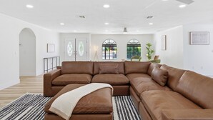 Un salon spacieux avec un grand canapé d’angle marron, un ventilateur de plafond, un éclairage encastré et une vue par la fenêtre.