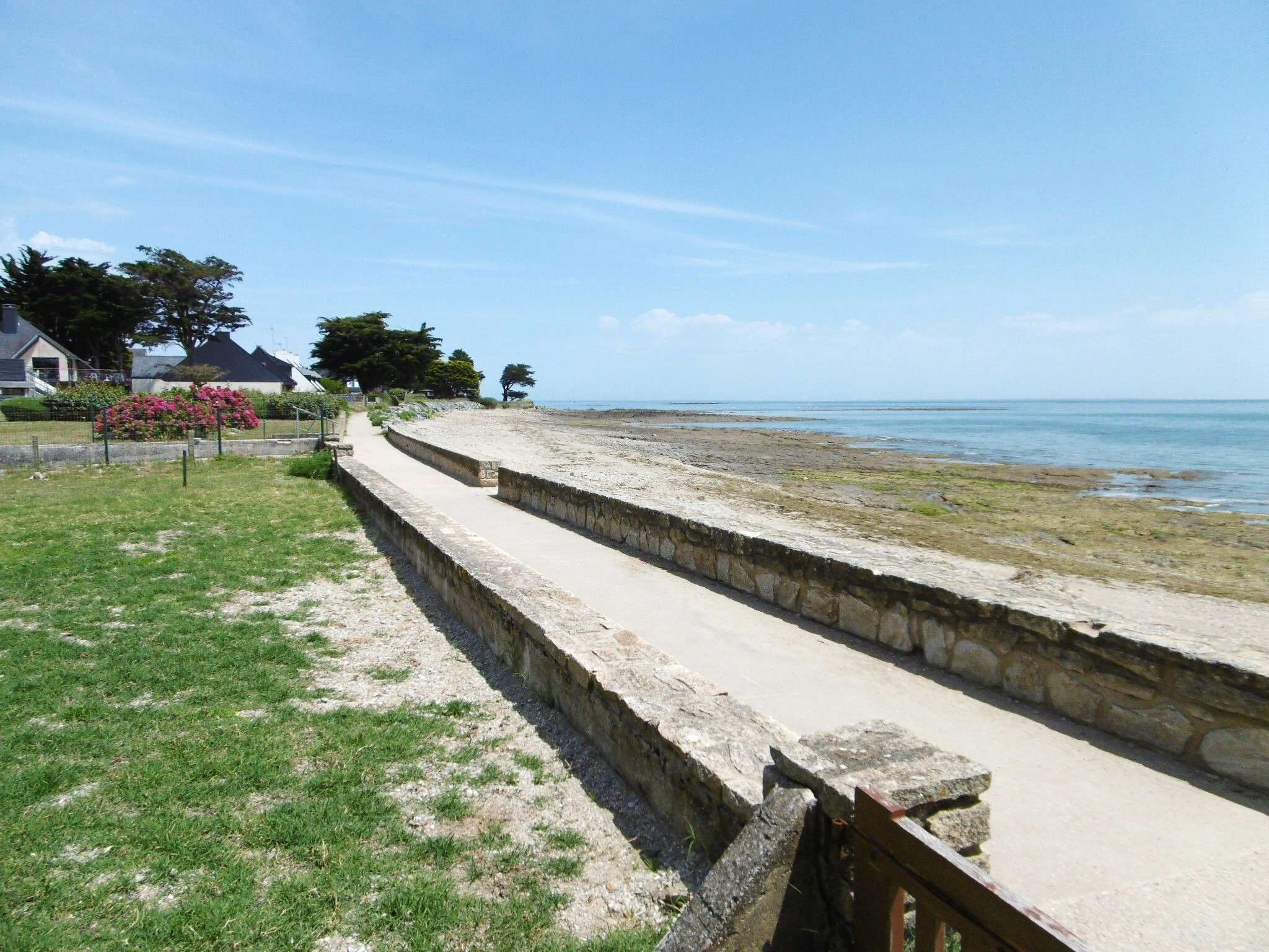 Un paseo marítimo con muro de piedra, zonas verdes y vista al mar.