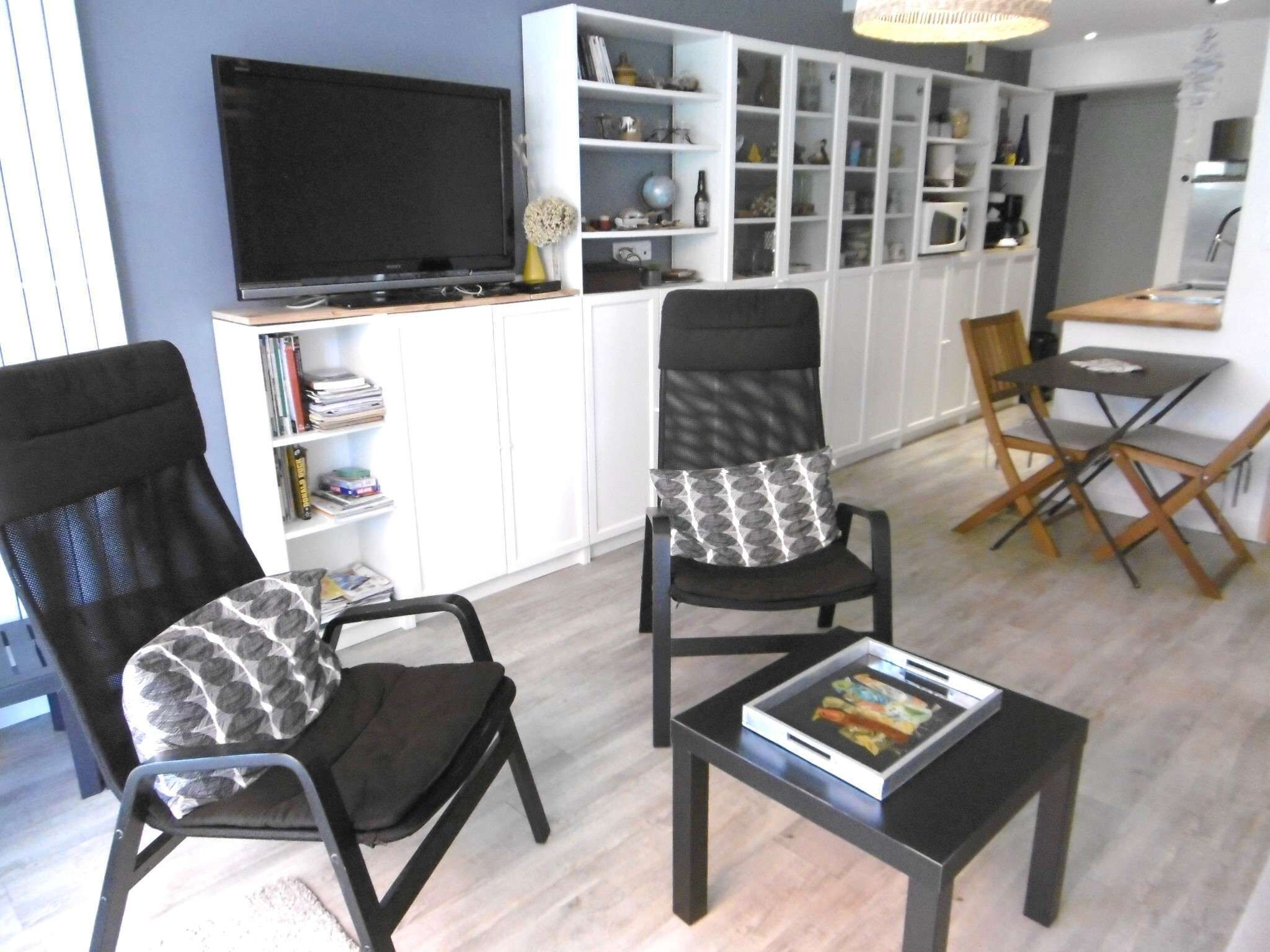 A living room with two black chairs, a black coffee table, a flat-screen TV, and a white cabinet with shelves.