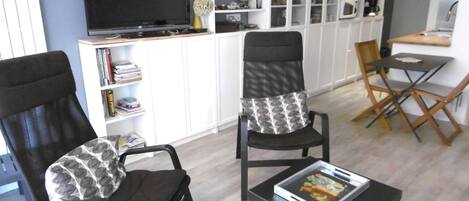 A living room with two black chairs, a black coffee table, a flat-screen TV, and a white cabinet with shelves.