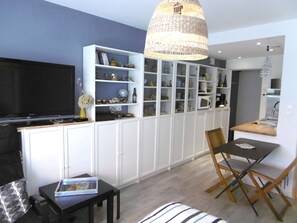 Ein kompakter Wohnbereich mit Küchenzeile, einer Essecke mit Tisch und Stühlen, einer Couch, einem Fernseher und einem Bücherregal.