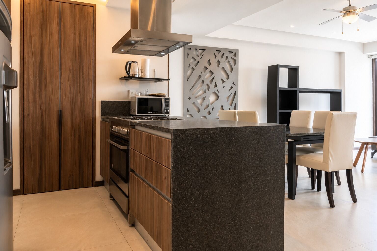 Una cocina moderna con una isla integrada, armarios de madera, electrodomésticos de acero inoxidable y una zona de comedor con mesa y sillas.