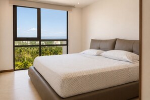 Ein Schlafzimmer mit großem Fenster, einem Bett mit Kopfteil und Blick auf Grünflächen und Gebäude.
