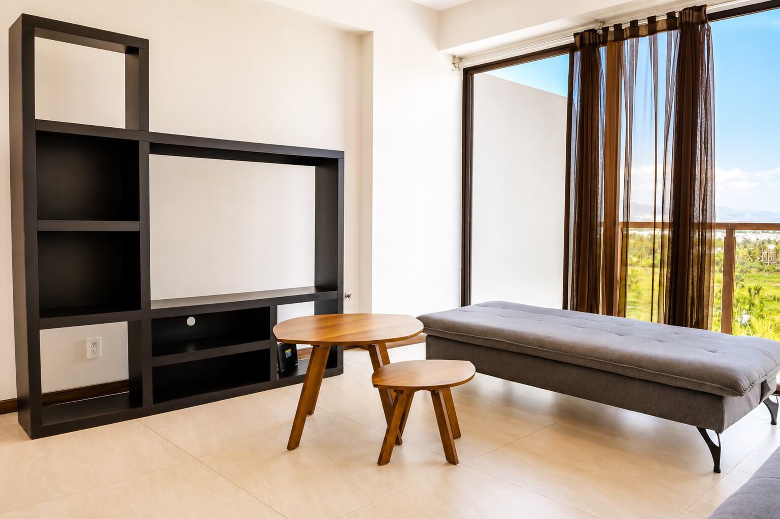 A modern room with a sofa, two small tables, a black shelving unit, and a large window with curtains.