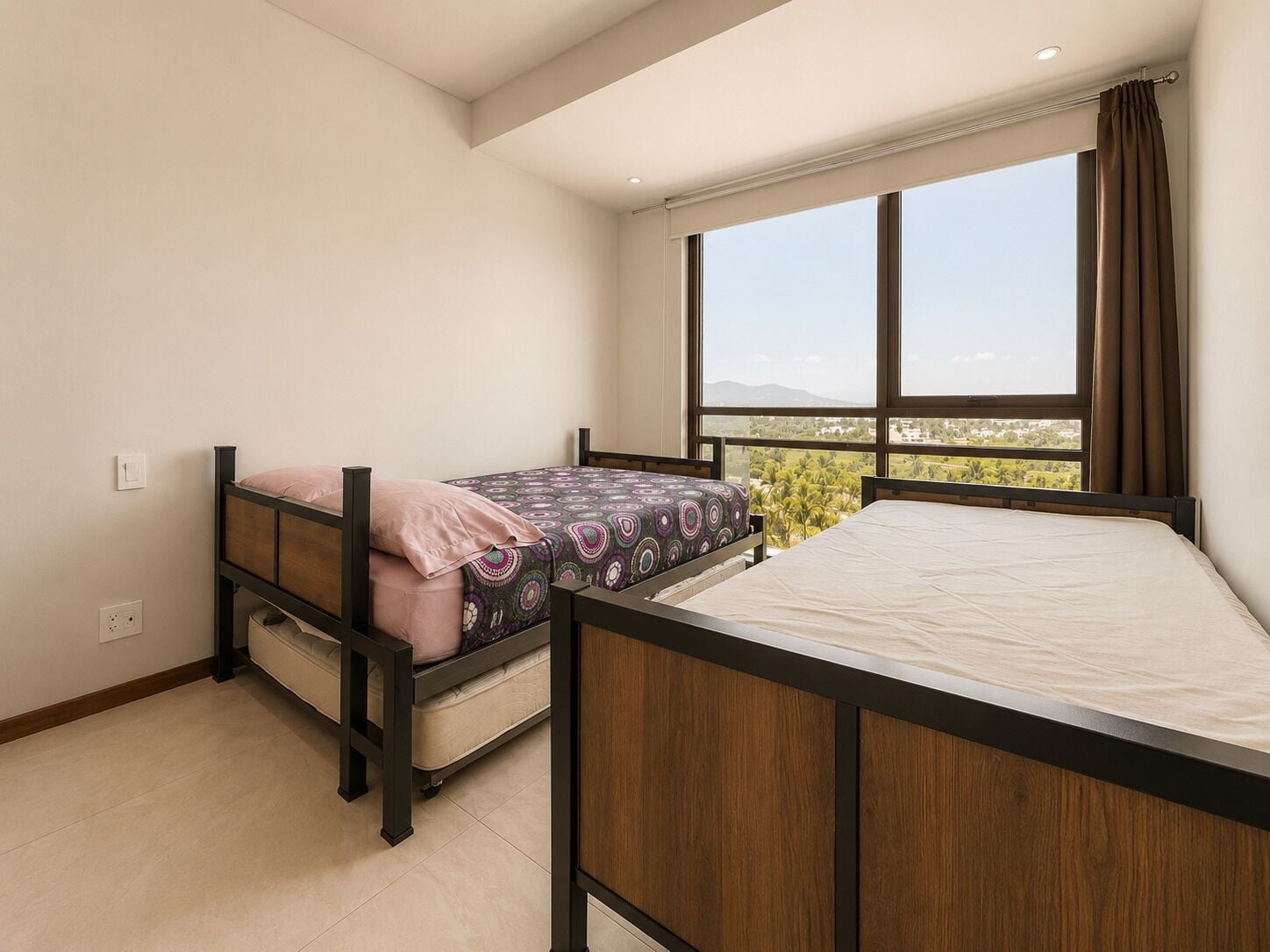 Quarto com cama beliche e uma cama de solteiro, uma janela grande com vista e uma luminária no teto.
