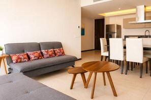 A modern living room with a grey sofa, patterned cushions, a wooden coffee table, and a dining area with white chairs and a black table. - Luxury Apartment & Pool in Acapulco 3BR (Acapulco)