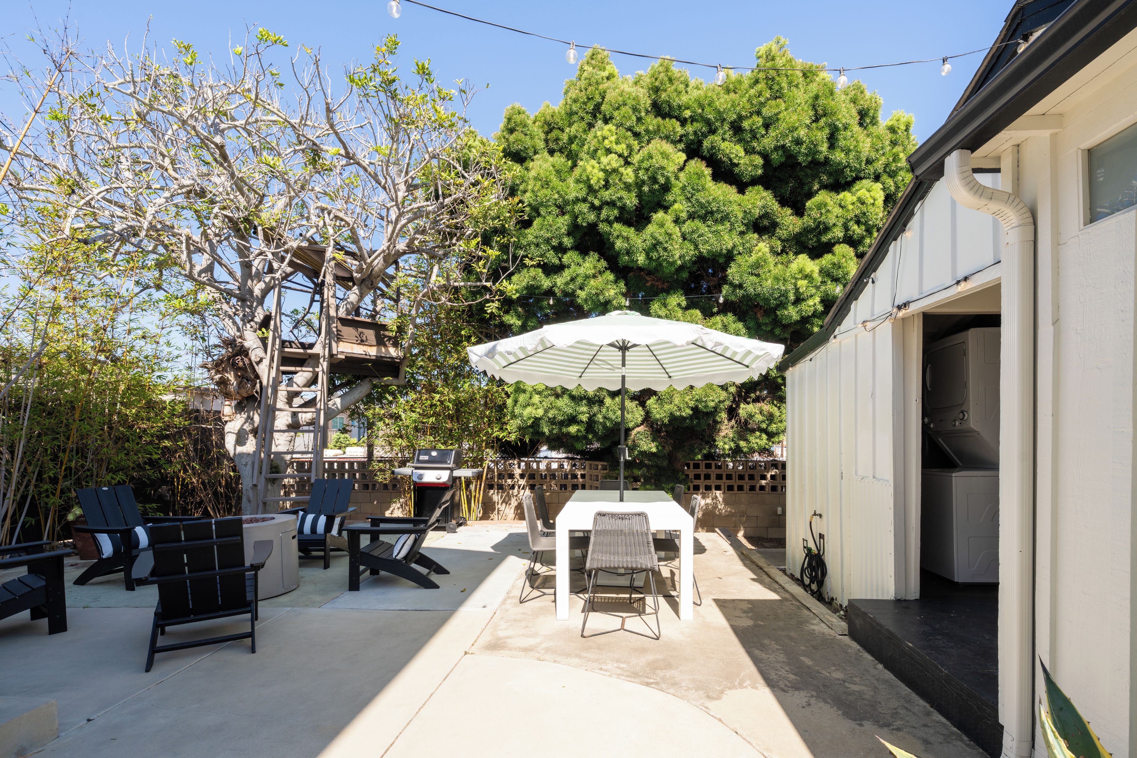 An outdoor patio area with a table and chairs, a barbecue grill, and a large umbrella.