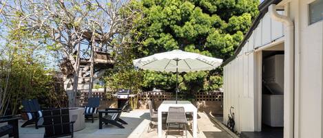 An outdoor patio area with a table and chairs, a barbecue grill, and a large umbrella.