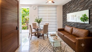 A modern living room with a glass coffee table, leather sofa, and a dining area with chairs and a vase of flowers. - Charming Studio Near Romantic Zone (Puerto Vallarta)