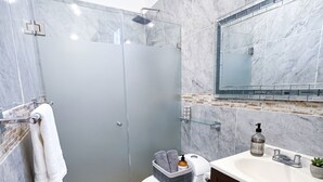 A modern bathroom with a glass-enclosed shower, a toilet, a sink with a mirror above, and a marble floor. - Charming Studio Near Romantic Zone (Puerto Vallarta)