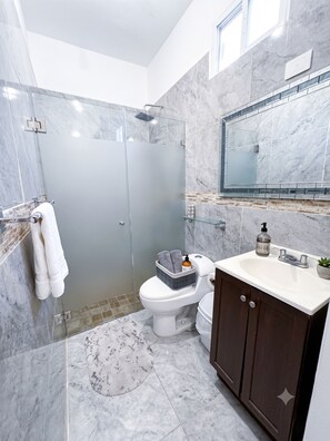 Een moderne badkamer met een douchecabine van glas, een toilet, een wastafel met spiegel erboven en een marmeren vloer.