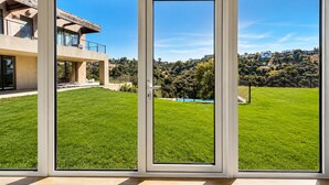 Una casa moderna con un amplio ventanal corredera, un césped cuidado y una vista despejada de una colina.