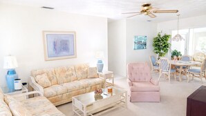 Uma sala de estar com sofá, poltrona, mesa de centro e um espaço de jantar com cadeiras e mesa.