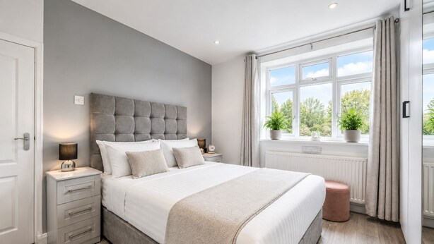 Un dormitorio con una cama grande, mesitas de noche, una mesita auxiliar, una ventana con cortinas y vistas al exterior.