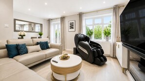 Una sala de estar moderna con un sofá, un sillón de masaje, un televisor y una ventana con plantas.