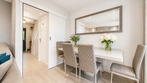 Un comedor con una mesa blanca, cuatro sillas, un espejo grande y un jarrón con flores.