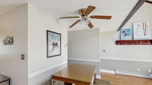 A dining area with a wooden table and chairs, a ceiling fan, and wall-mounted ski-themed artwork. - Cozy 3BR Condo - Fireplace - Tannersville (Pennsylvania)