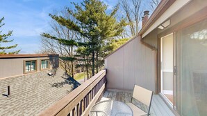 A balcony with a table and chairs, a view of trees, and a building with a window. - Cozy 3BR Condo - Fireplace - Tannersville (Pennsylvania)