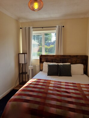 A bedroom with a large bed, a window with curtains, a radiator, and a bedside table with a lamp. - Perfect for Professionals,Visitors &Extended Stays near Qmc,Warhammer,University (Nottingham)