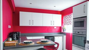 Une cuisine avec des meubles blancs, un mur rouge et un four encastré.