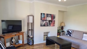 Un salon équipé d’un téléviseur à écran plat, d’une table basse en bois, d’un canapé, d’une lampe sur pied et d’un cadre photo fixé au mur.