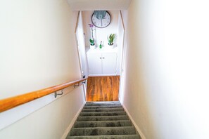 A staircase with a wooden handrail, a clock on the wall, and potted plants on the landing. - Perfect for Professionals,Visitors &Extended Stays near Qmc,Warhammer,University (Nottingham)