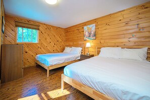 Quarto com duas camas de madeira, uma janela, um quadro e um abajur.
